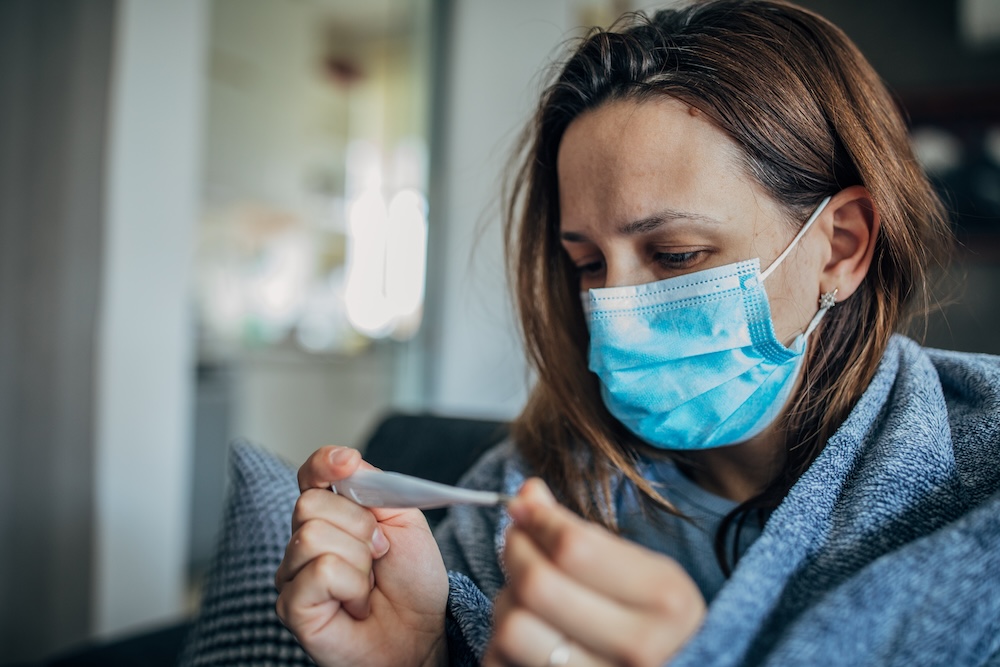 woman wearing mask looking at a thermometer