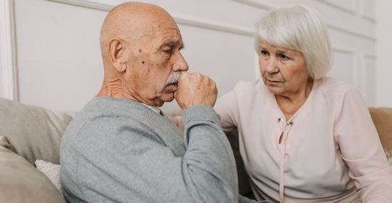 Older man coughing while wife watches