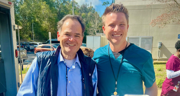 two men posing for a photo outside